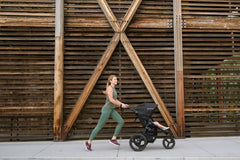Mother jogging with Bumbleride Australia Speed Jogging Stroller in Black on sidewalk with wood wall in background
