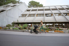Mother jogging with Bumbleride Australia Speed Jogging Stroller in Black on sidewalk with cement building and succulent plants in background